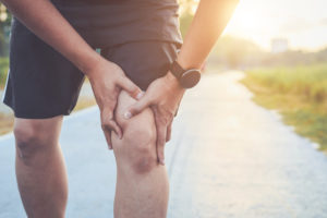 Injury from workout concept : Asian man use hands hold on his knee while running on road in the park. Shot in morning time, sunlight and warm effect with copy space for text or design